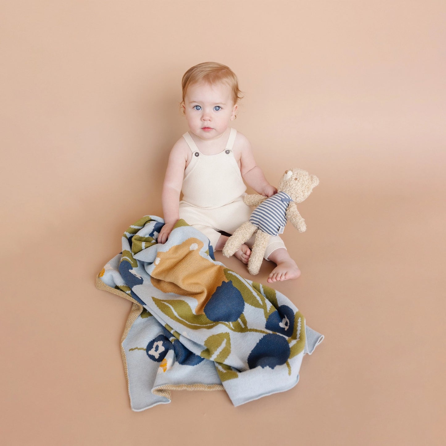 Baby sitting on a floral blanket holding a toy, with a beige background