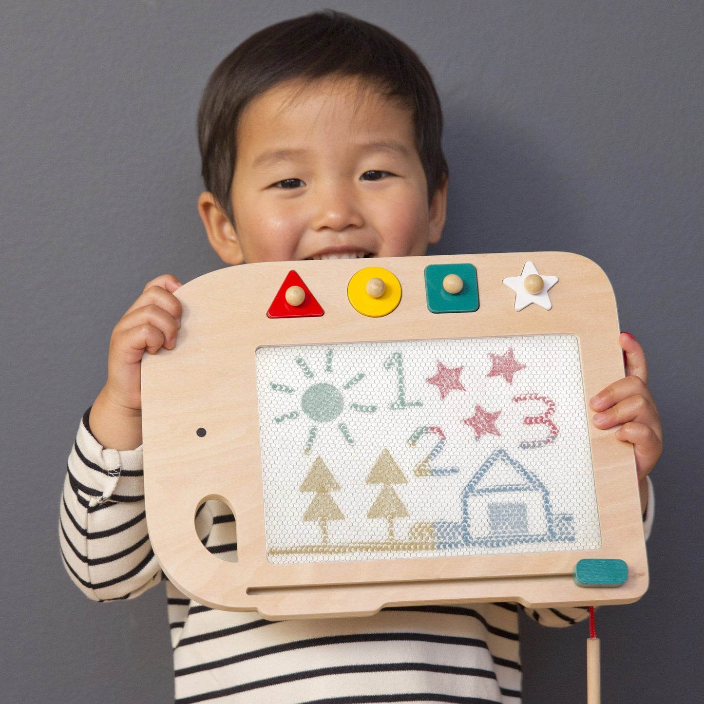 Child holding a wooden toy with colorful buttons and drawings on a gray background