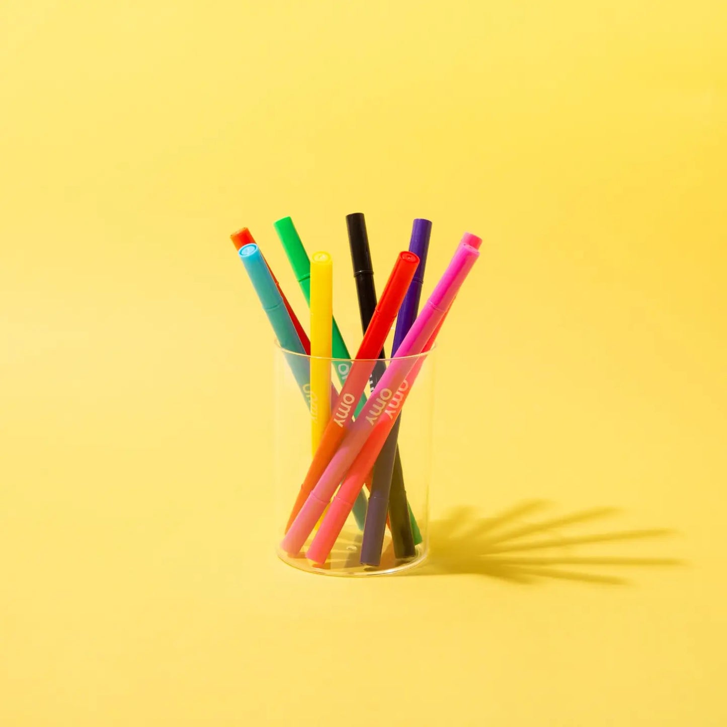 Colorful markers in a clear glass on a yellow background