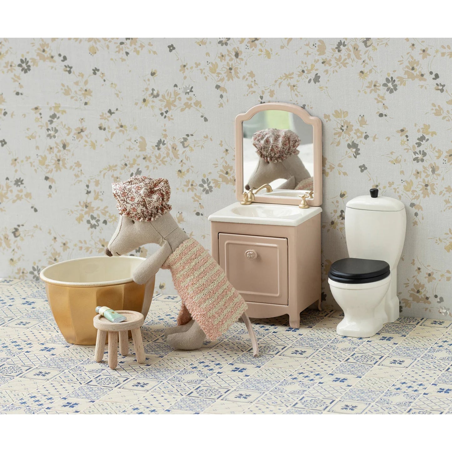 Children's bathroom set with toy mouse, bathtub, sink, and toilet against a floral wallpaper background.