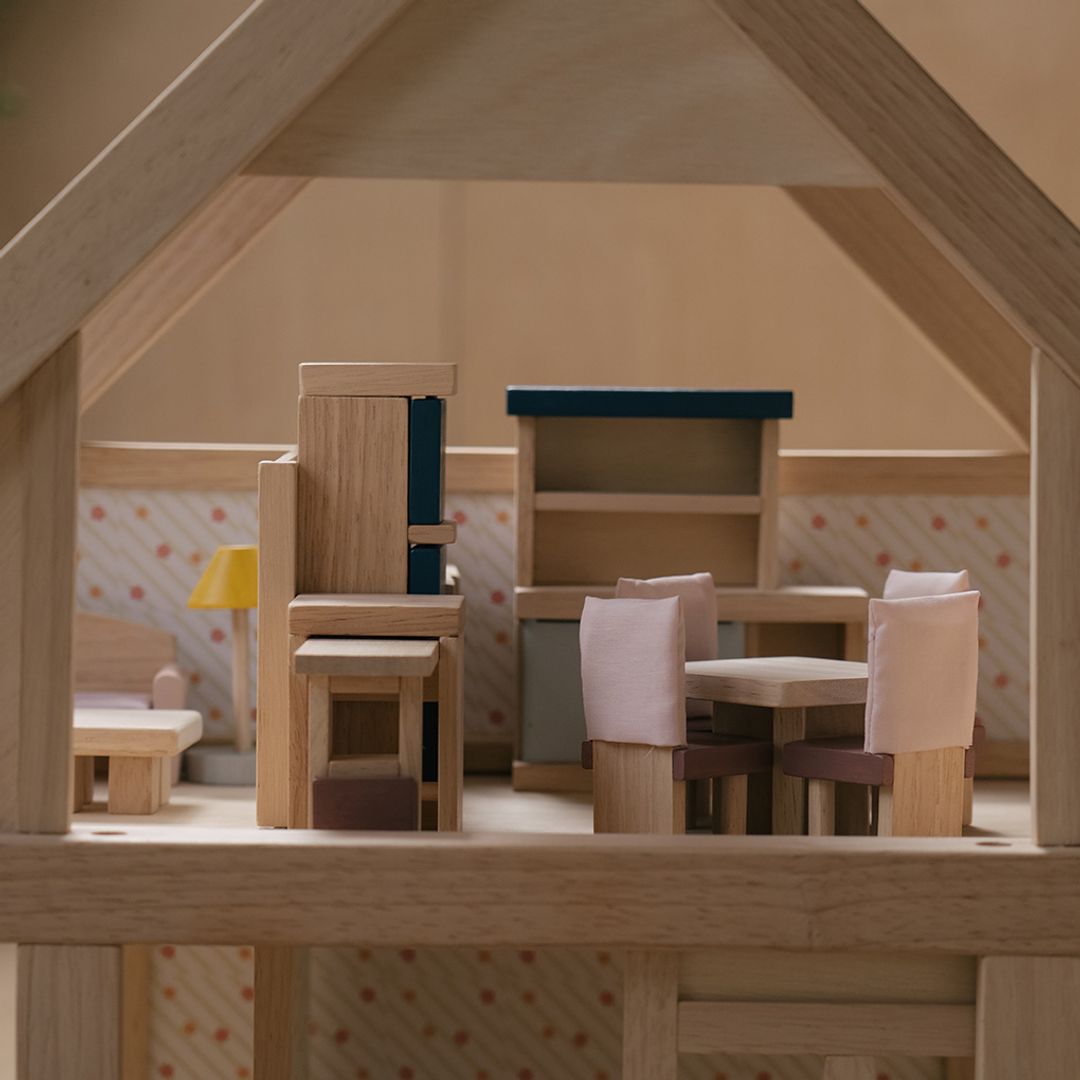Wooden dollhouse furniture including chairs and a table inside a dollhouse.