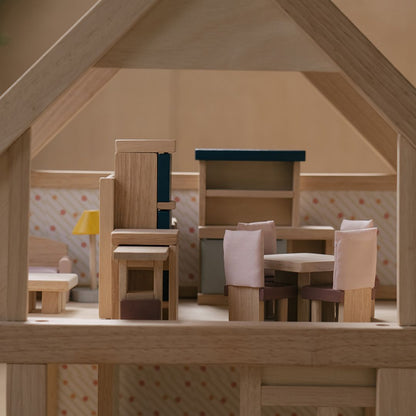 Wooden dollhouse furniture including chairs and a table inside a dollhouse.
