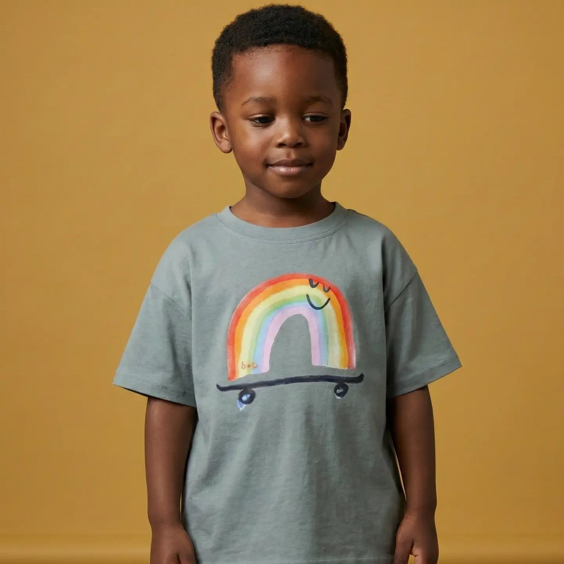 Child wearing a gray t-shirt with a colorful rainbow design on a green background