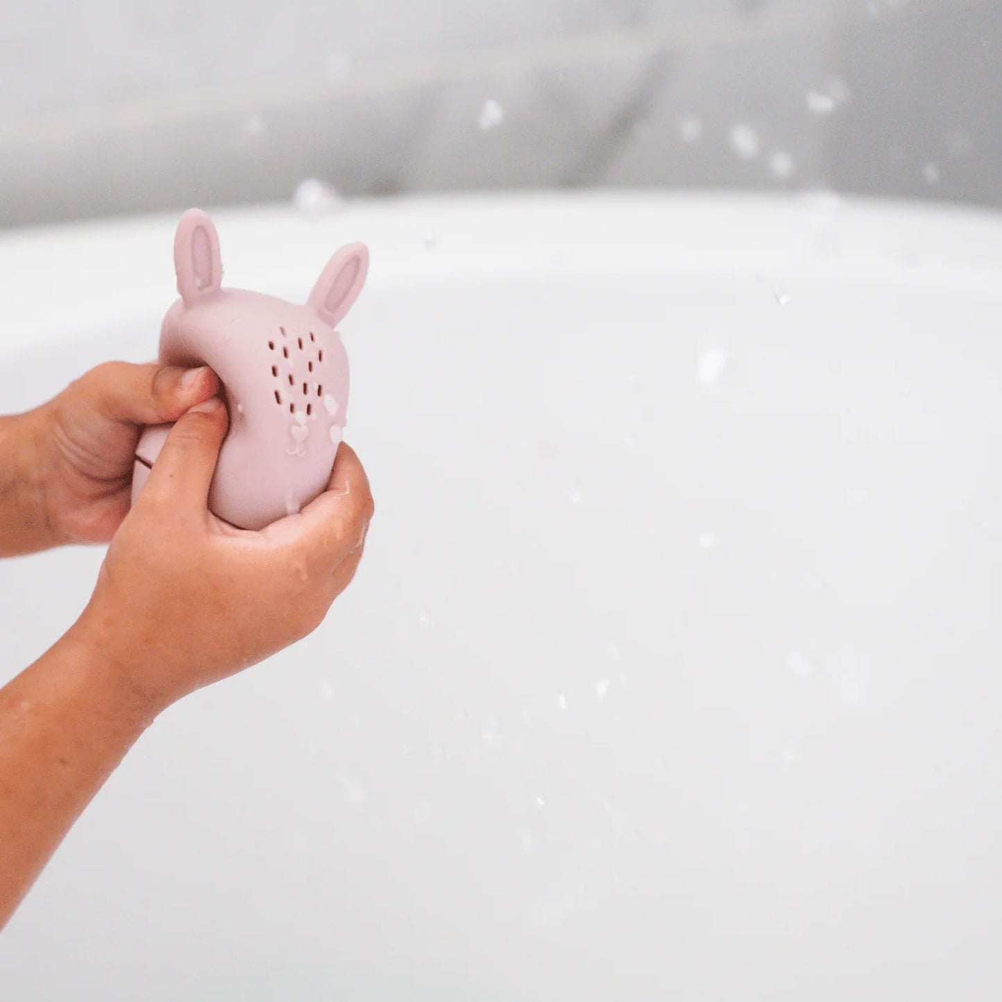 Hand holding a pink rabbit-shaped bath toy against a white background