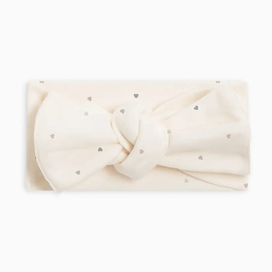 An off-white fabric headband with a large bow and small metallic silver heart details, displayed on a clean white background.