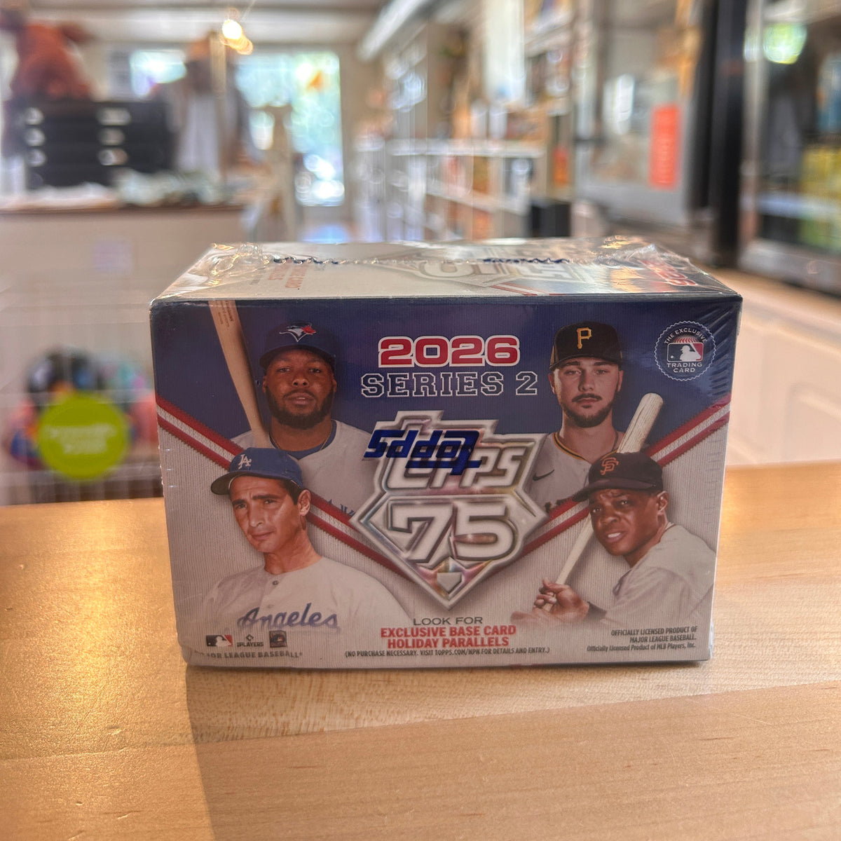 A sealed 2026 Series 2 Topps 75 baseball card mini box sits on a wooden counter in a blurred retail store environment.