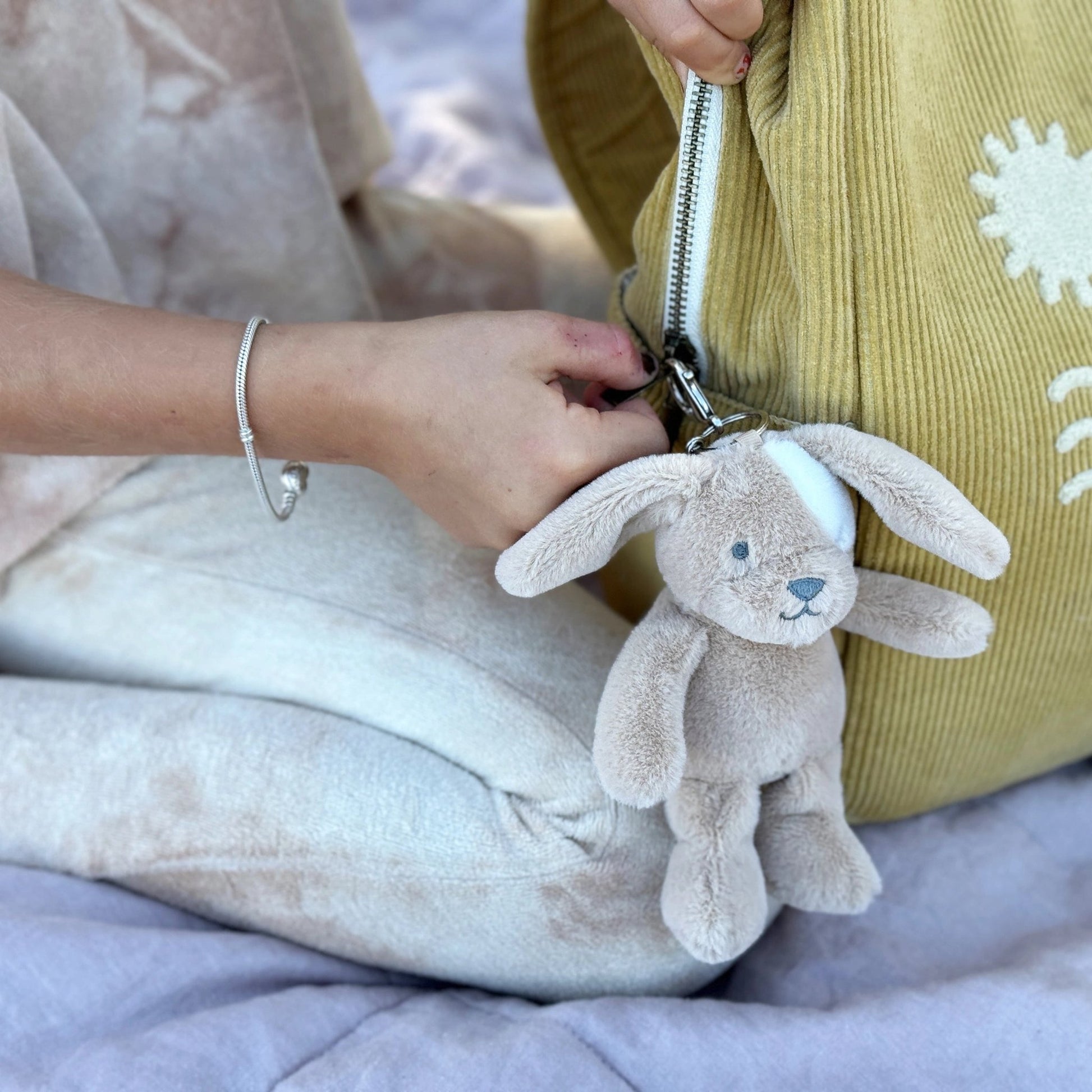 Person holding a plush bunny keychain with a yellow bag featuring white patterns.