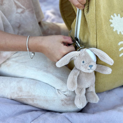 Person holding a plush bunny keychain with a yellow bag featuring white patterns.