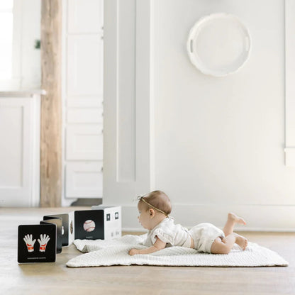 Baby lying on a white rug in a minimalistic room with products displayed.