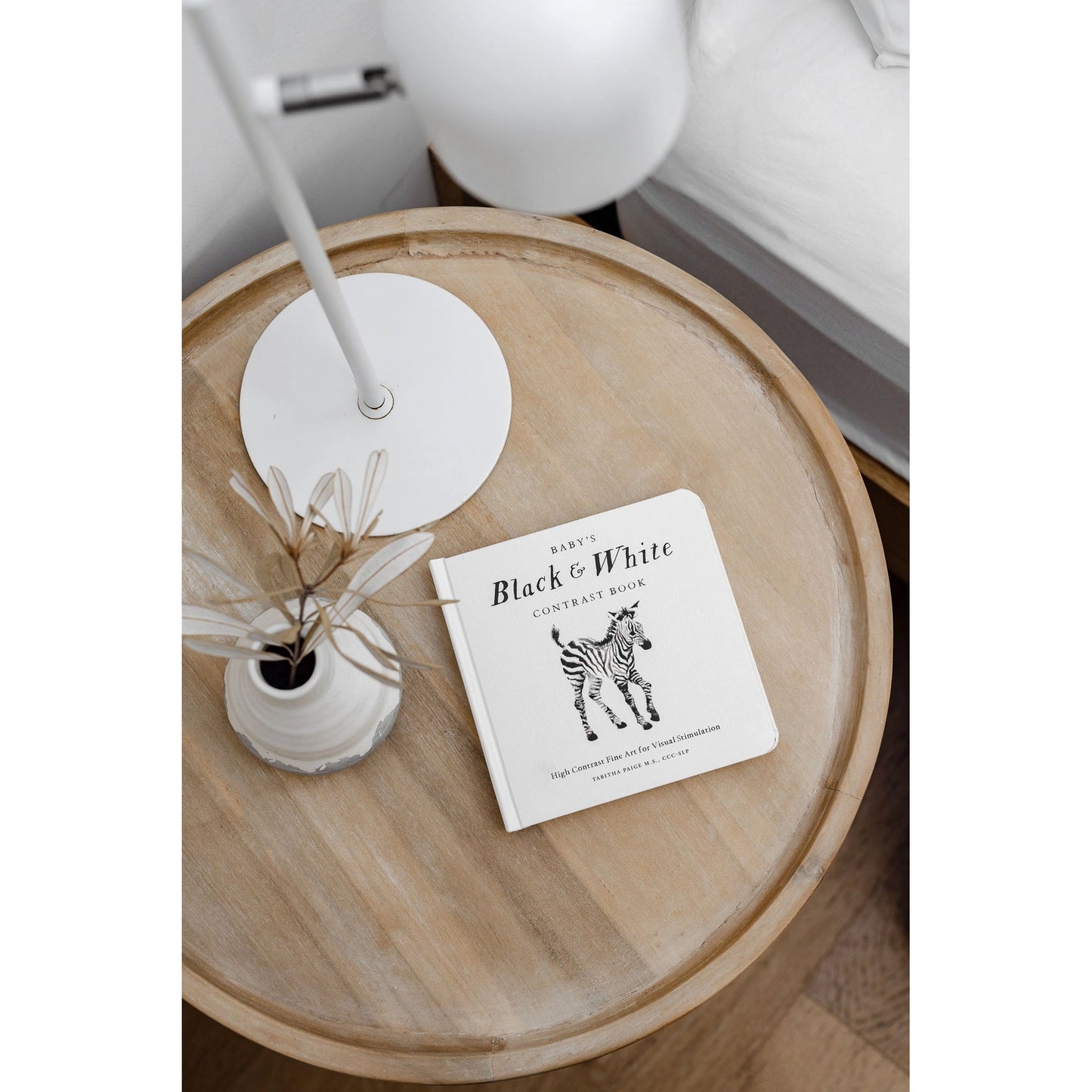 Round wooden table with a book titled 'Black & White' and a small plant on a white background