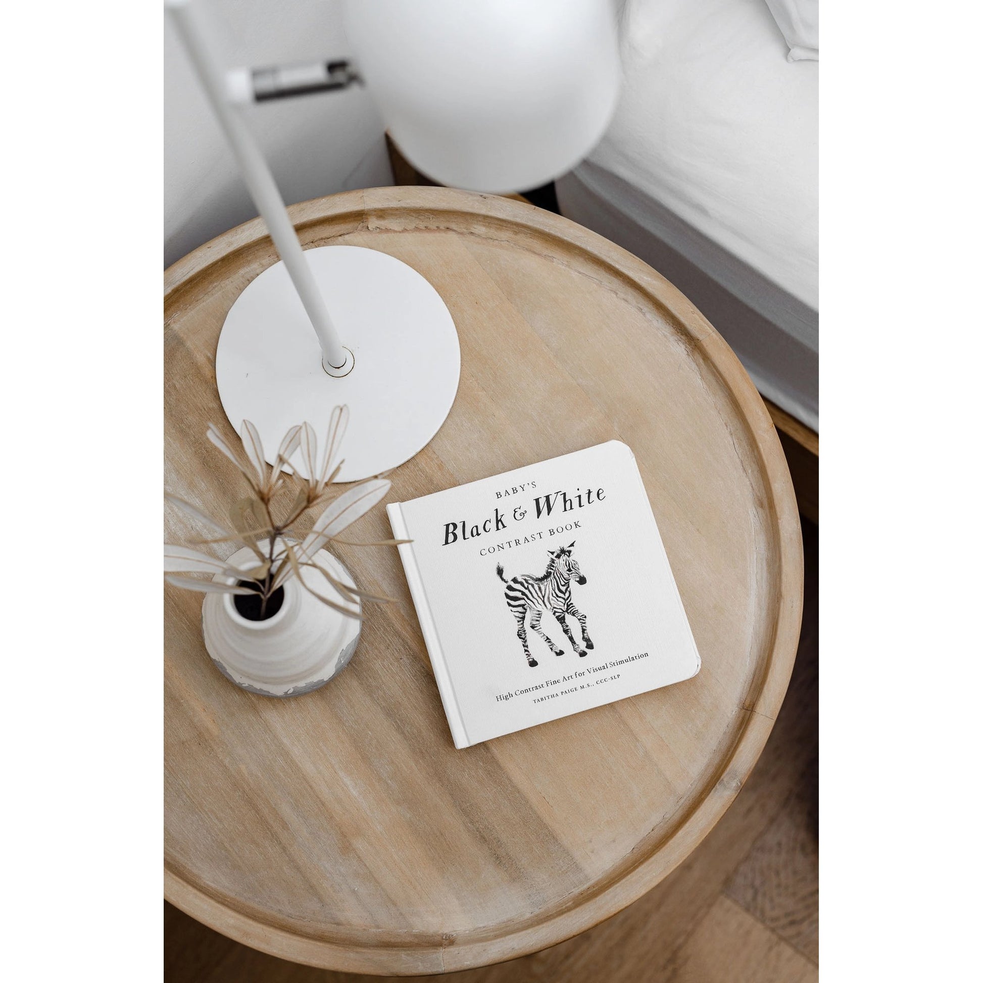 Round wooden table with a book titled 'Black & White' and a small plant on a white background