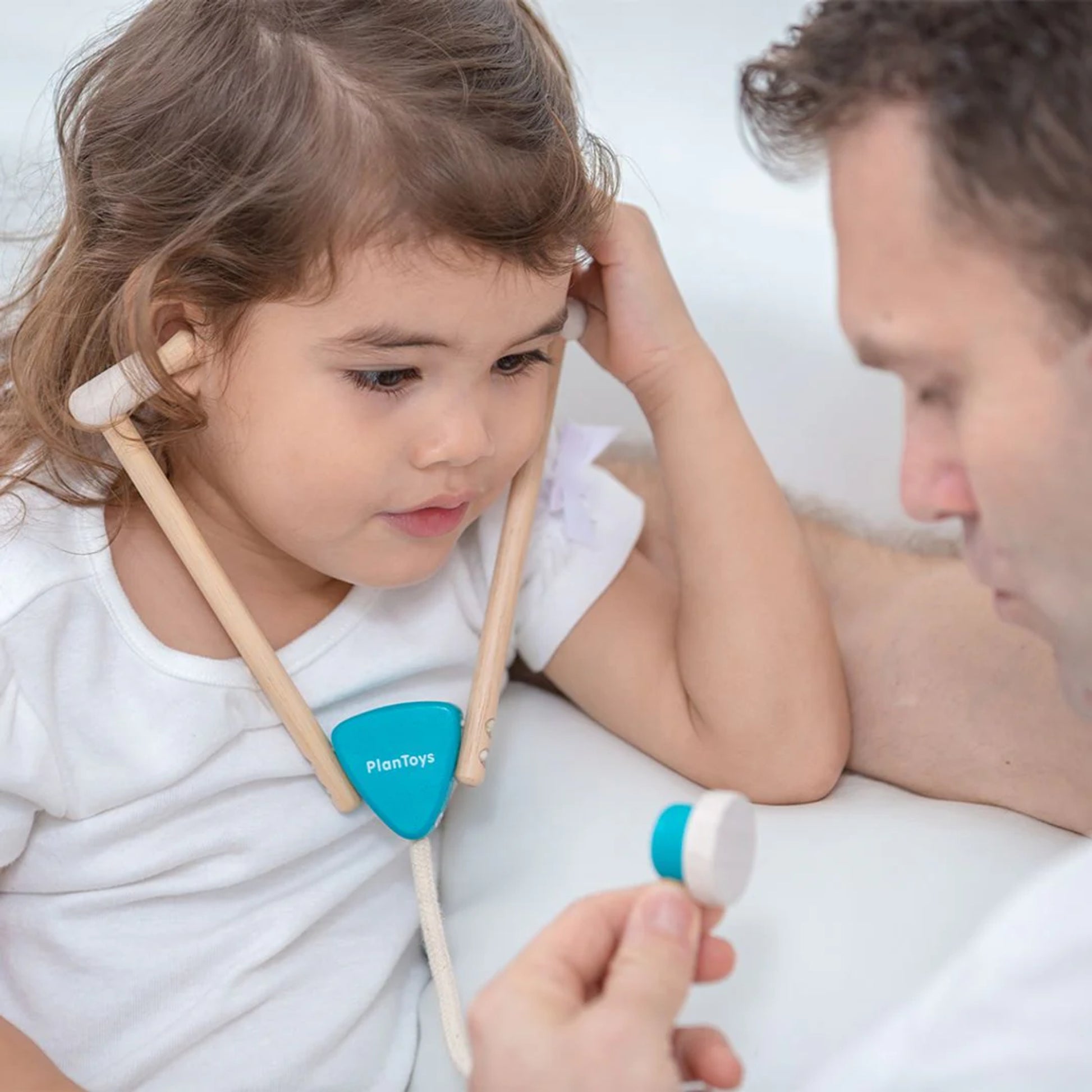 Child playing with a toy stethoscope held by an adult against a white background