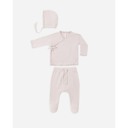 A baby clothing set in a very pale blush pink, including a long-sleeve wrap-style top with lace trim, matching footed pants with a drawstring, and a bonnet, laid out on a light gray background.