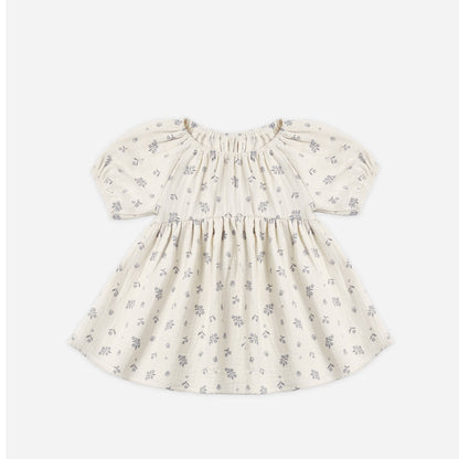 A baby girl's short-sleeve dress in cream cotton fabric with a delicate gray floral print, featuring a smocked bodice and puffed sleeves, shown flat on a light gray background.