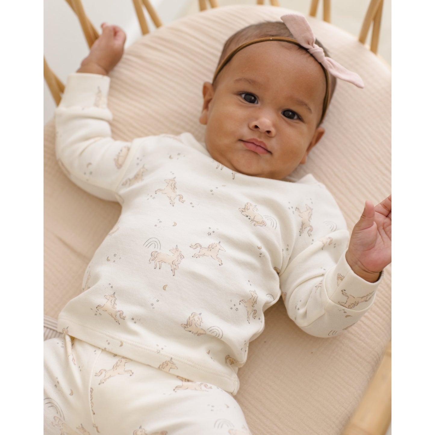 Baby lying on a cushion wearing a white outfit with animal prints and a pink headband.