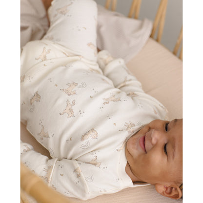 Baby lying in a crib wearing a white outfit with small patterns, smiling.