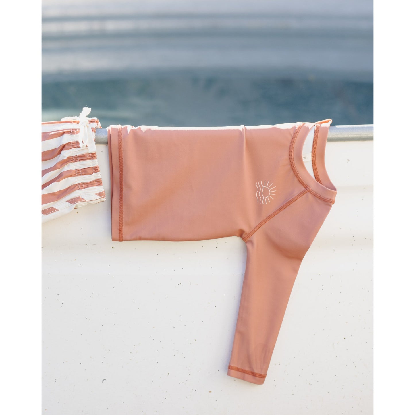 poppy colored swimsuit with a sun design hanging on a railing by the water.