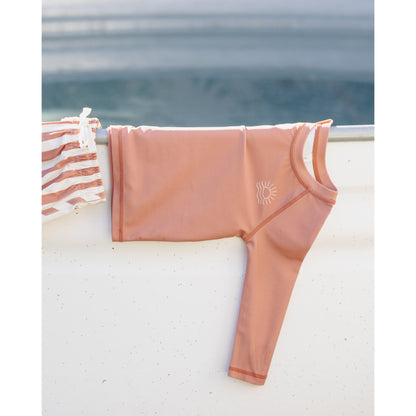 poppy colored swimsuit with a sun design hanging on a railing by the water.