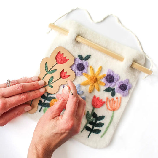 Handmade floral design on a felt board with a person holding a wooden flower piece.