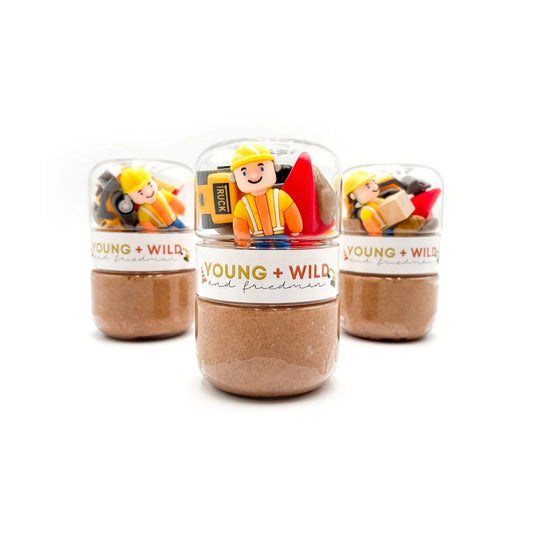 Three small clear dome-shaped jars filled with brown powder or granules, each topped with a colorful construction-themed label and small toy figure, on a white background.