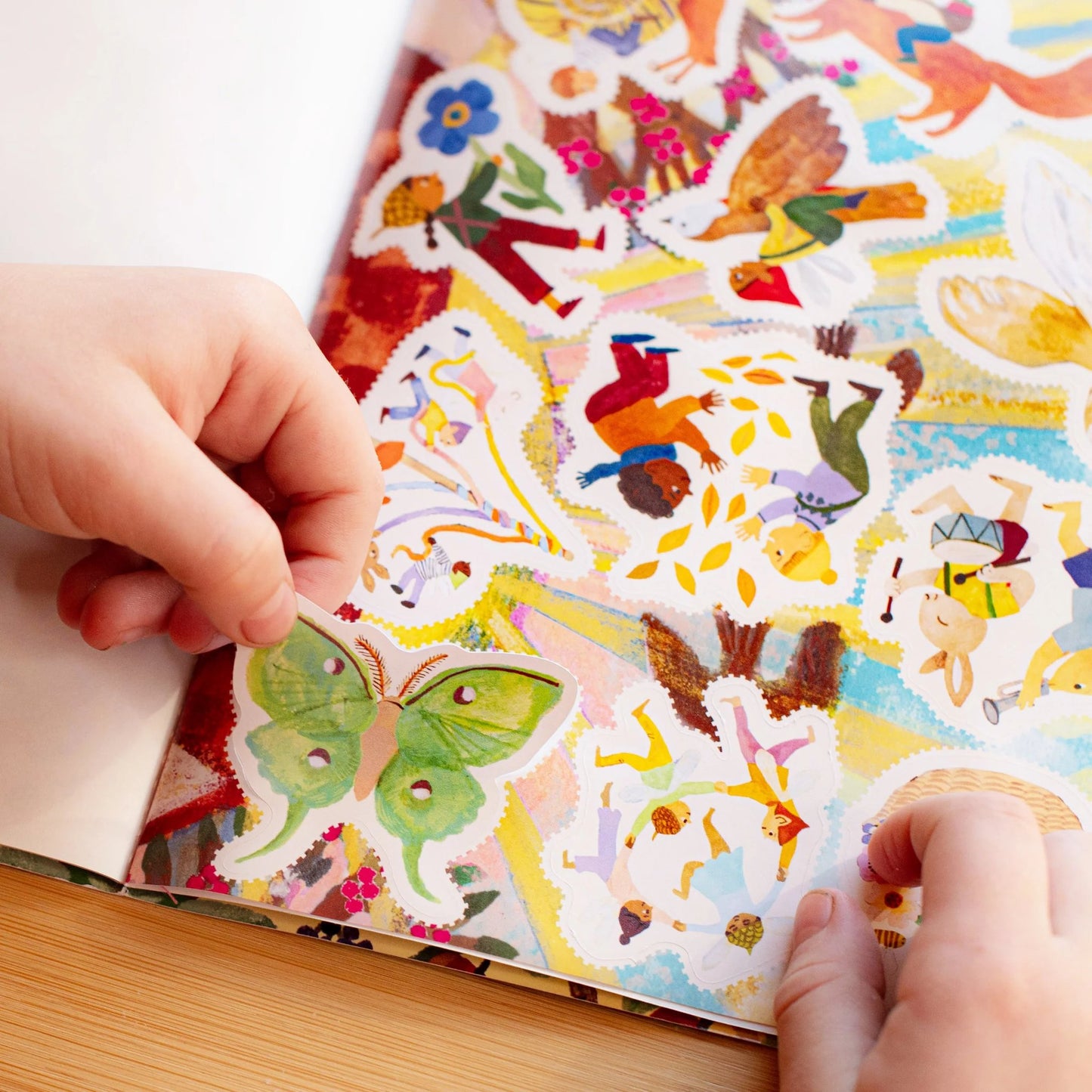 Colorful sticker book with various illustrations, held open by a hand on a wooden surface.