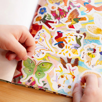 Colorful sticker book with various illustrations, held open by a hand on a wooden surface.