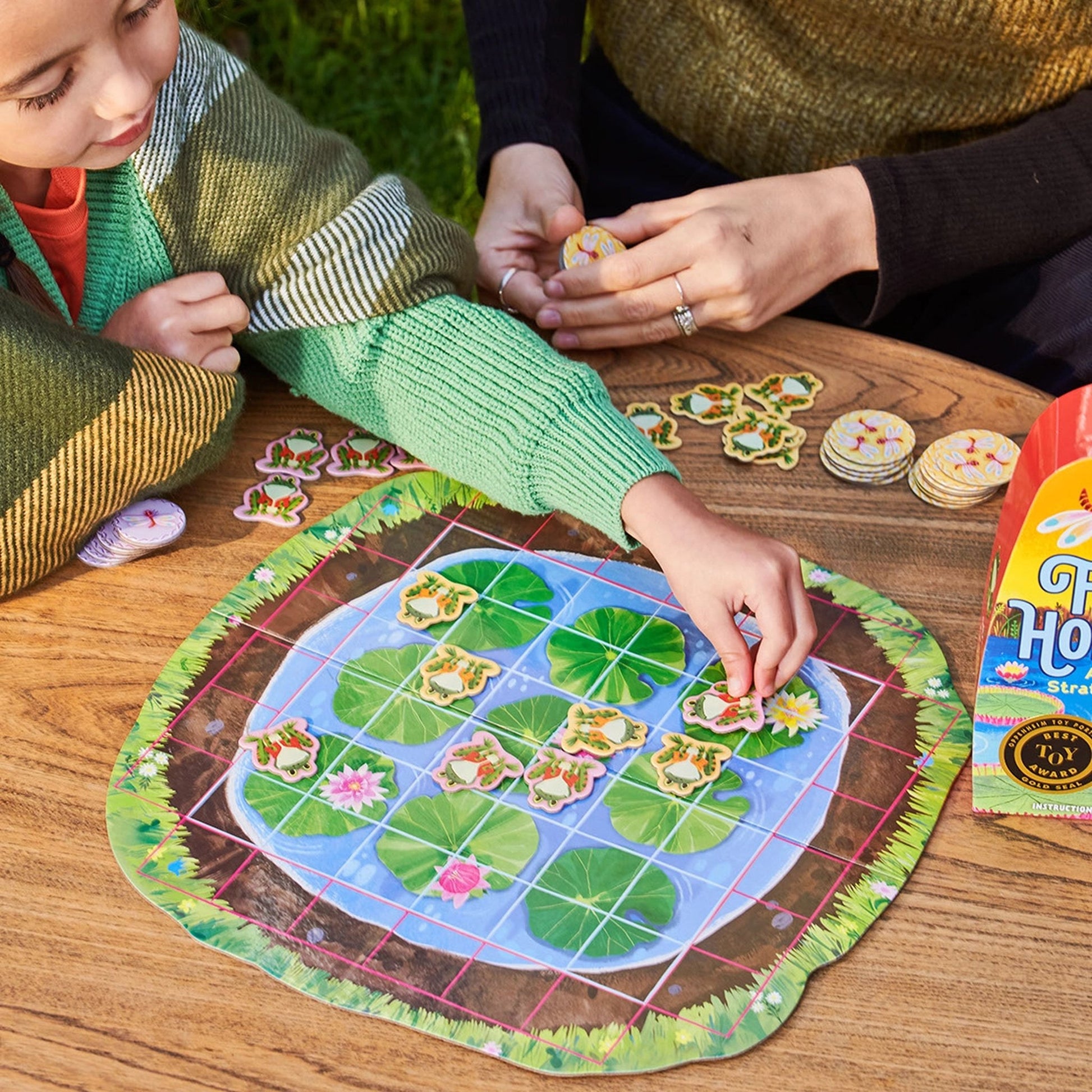 Two children playing a board game with a nature-themed board on a wooden table.