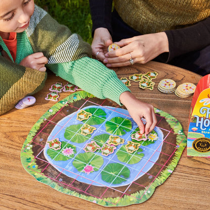 Two children playing a board game with a nature-themed board on a wooden table.