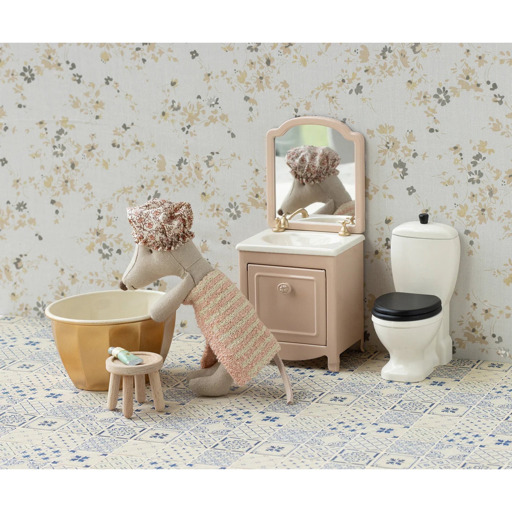 Children's bathroom set with toy mouse, bathtub, sink, and toilet against a floral wallpaper background.